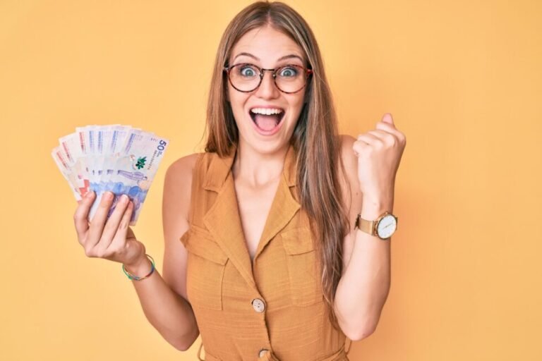 young blonde girl holding colombian pesos screaming proud, celebrating victory and success very excited with raised arms